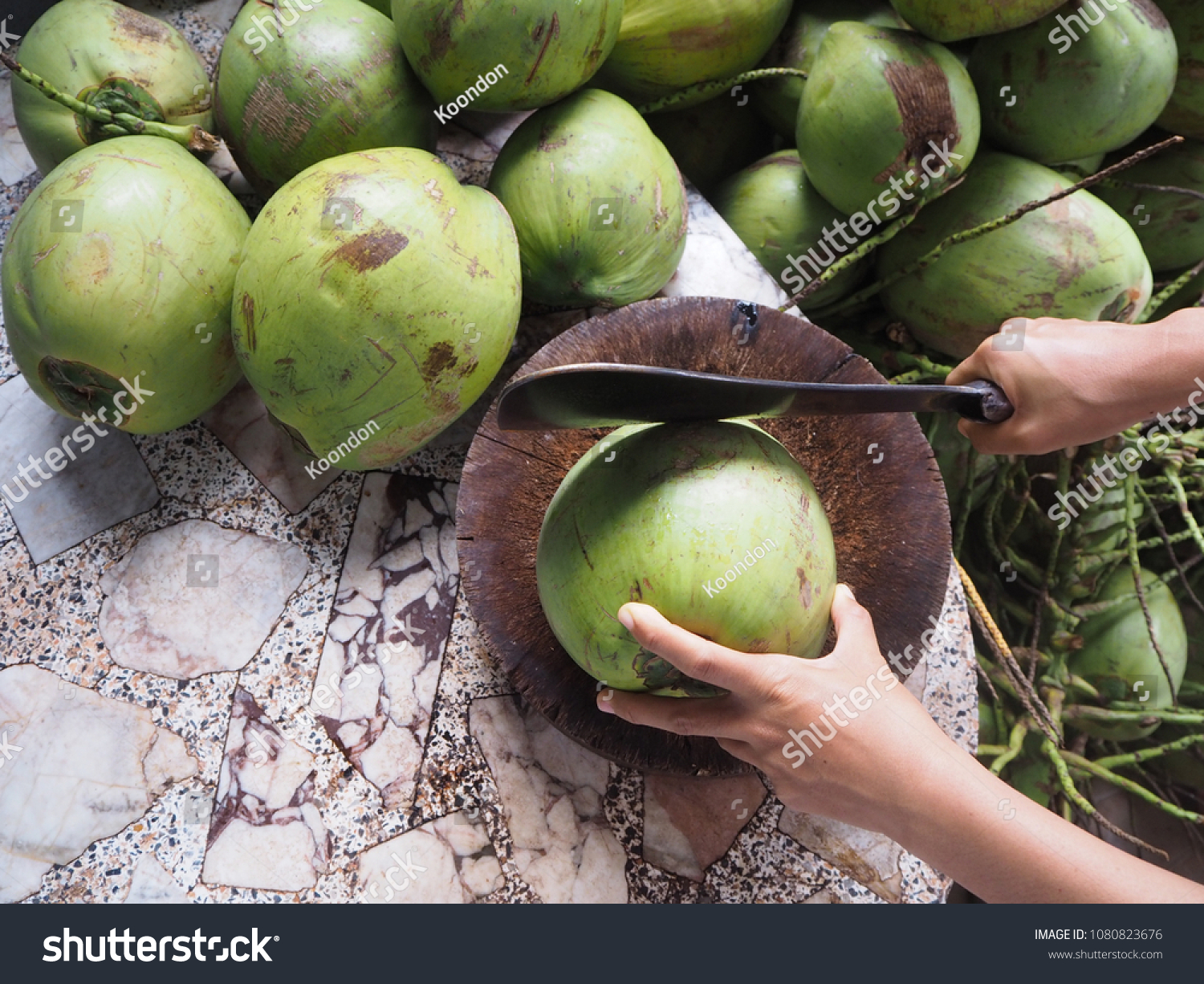Man using knife to chopped fresh coconut for drink and green coconuts background top view.