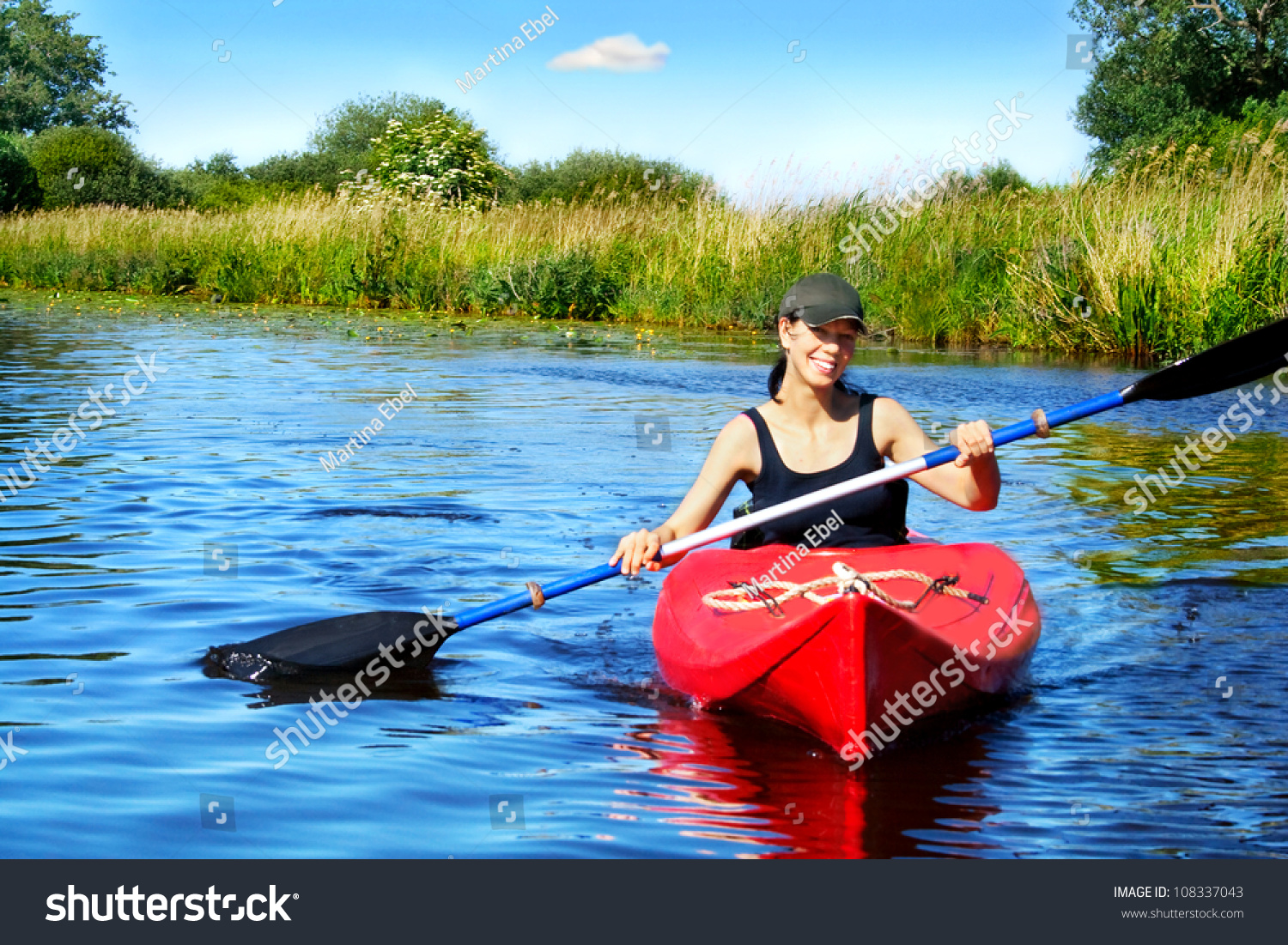 Girl with paddle and kayak on a small river in rural landscape
