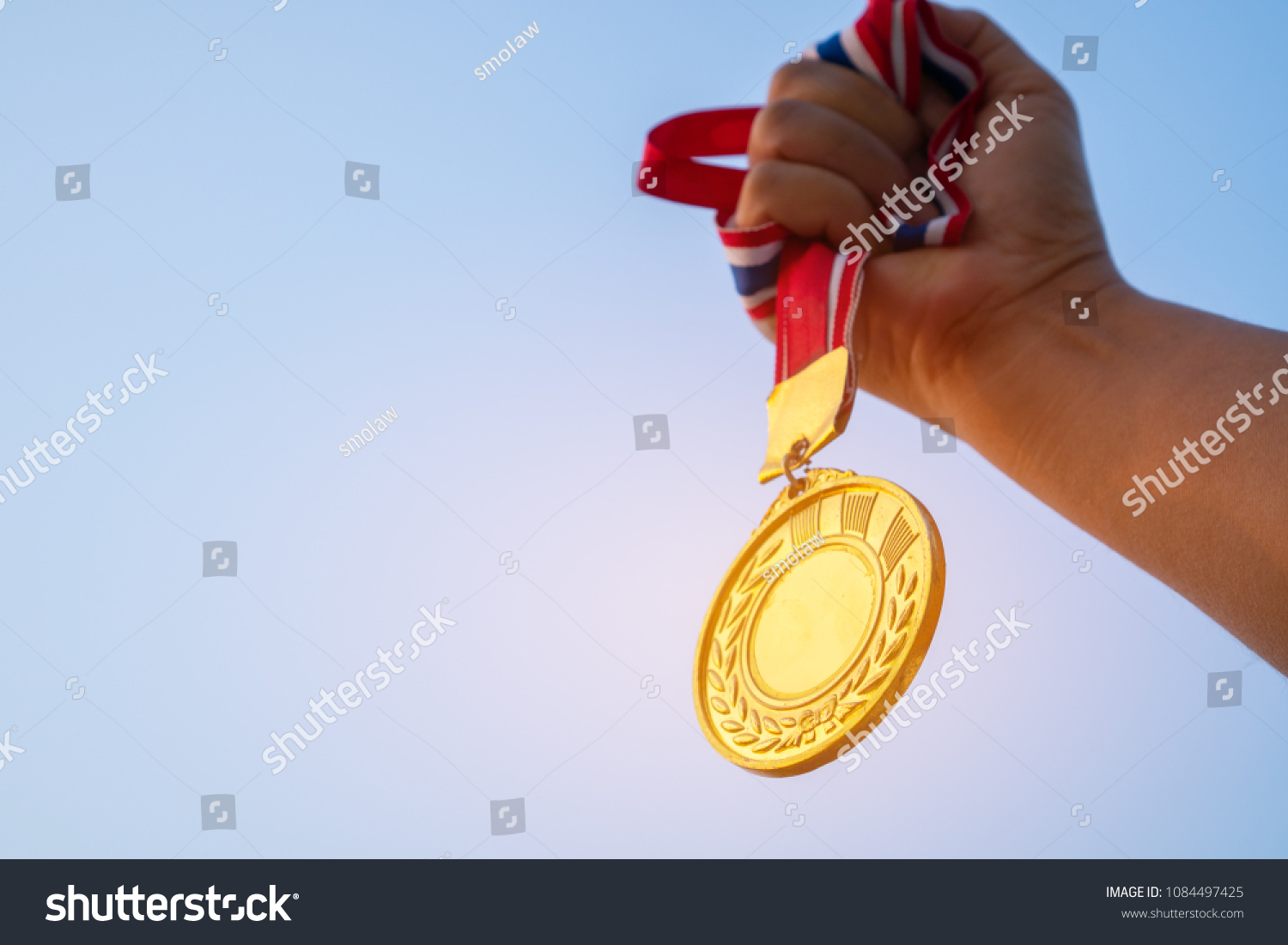 Winners Champion in success award concept : Woman hands raised holding gold medals with ribbon against blue sky background to show success in sport or business