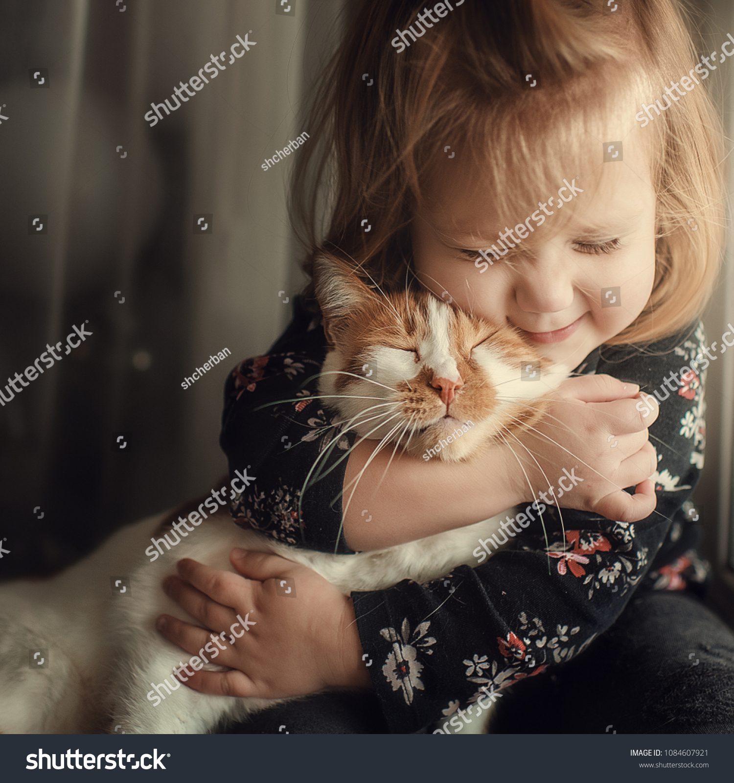 Portrait of a small cute child with a bald head that embraces with tenderness and love a red cat and smiles with happiness