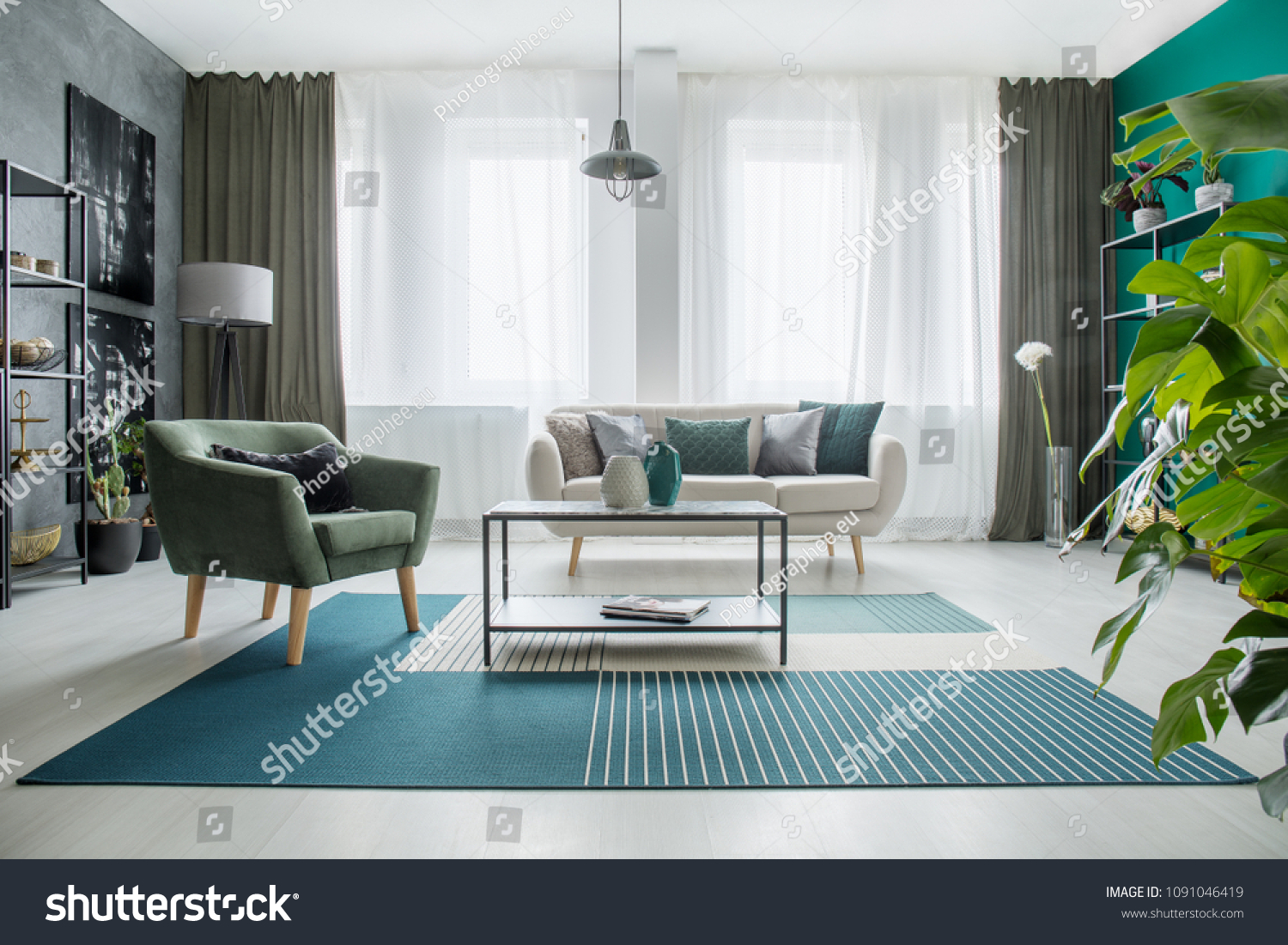 Table on carpet next to a green armchair and beige sofa in bright living room interior with plant