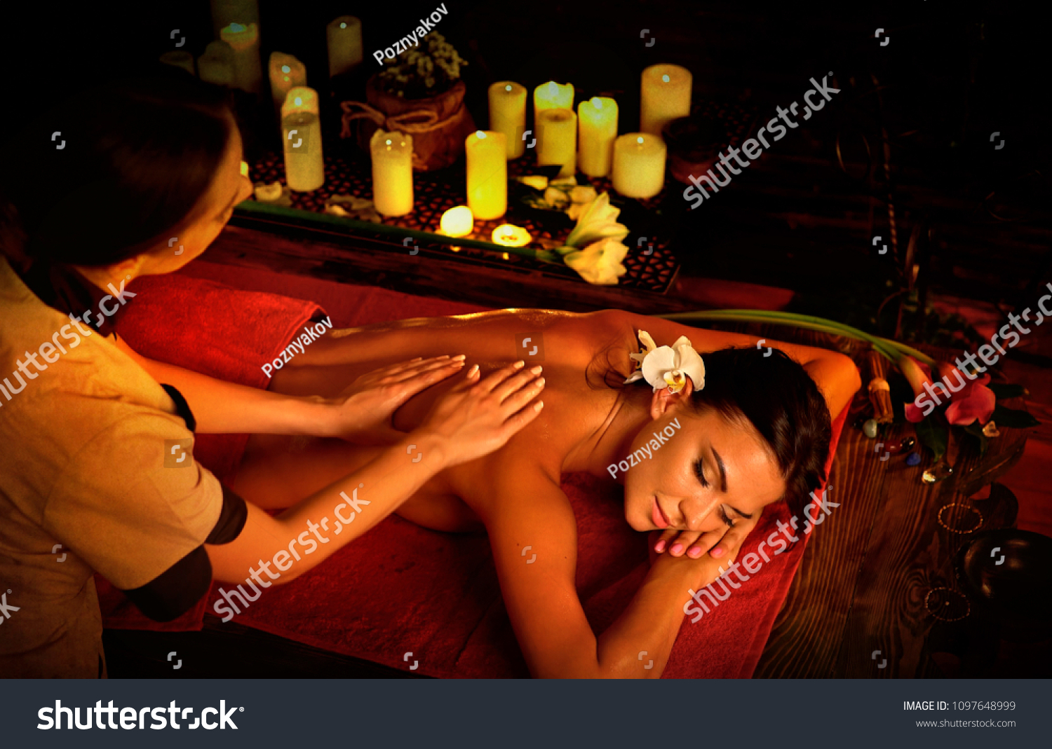 Massage of woman in spa salon. Girl on candles background treats problem nack and sholders. Luxary interior with working hands masseuse. Crop of bare back has relax. Alternative medicine on very dark