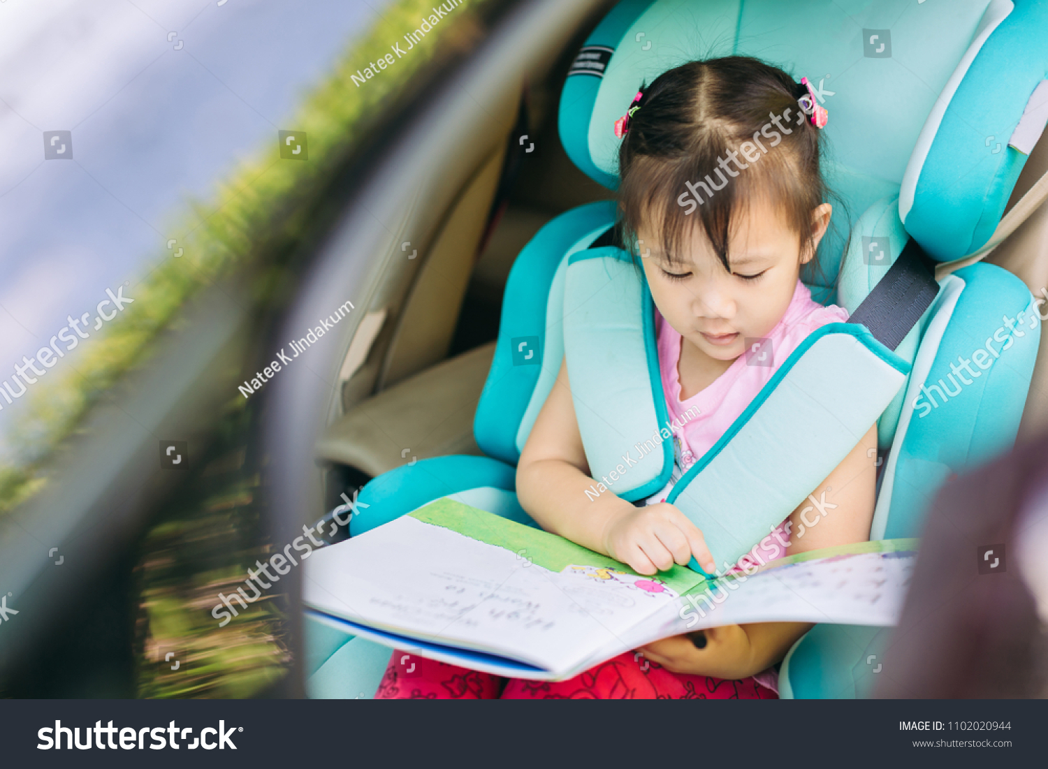 kid reading a book wait for mother and sit in the car seat for safety.