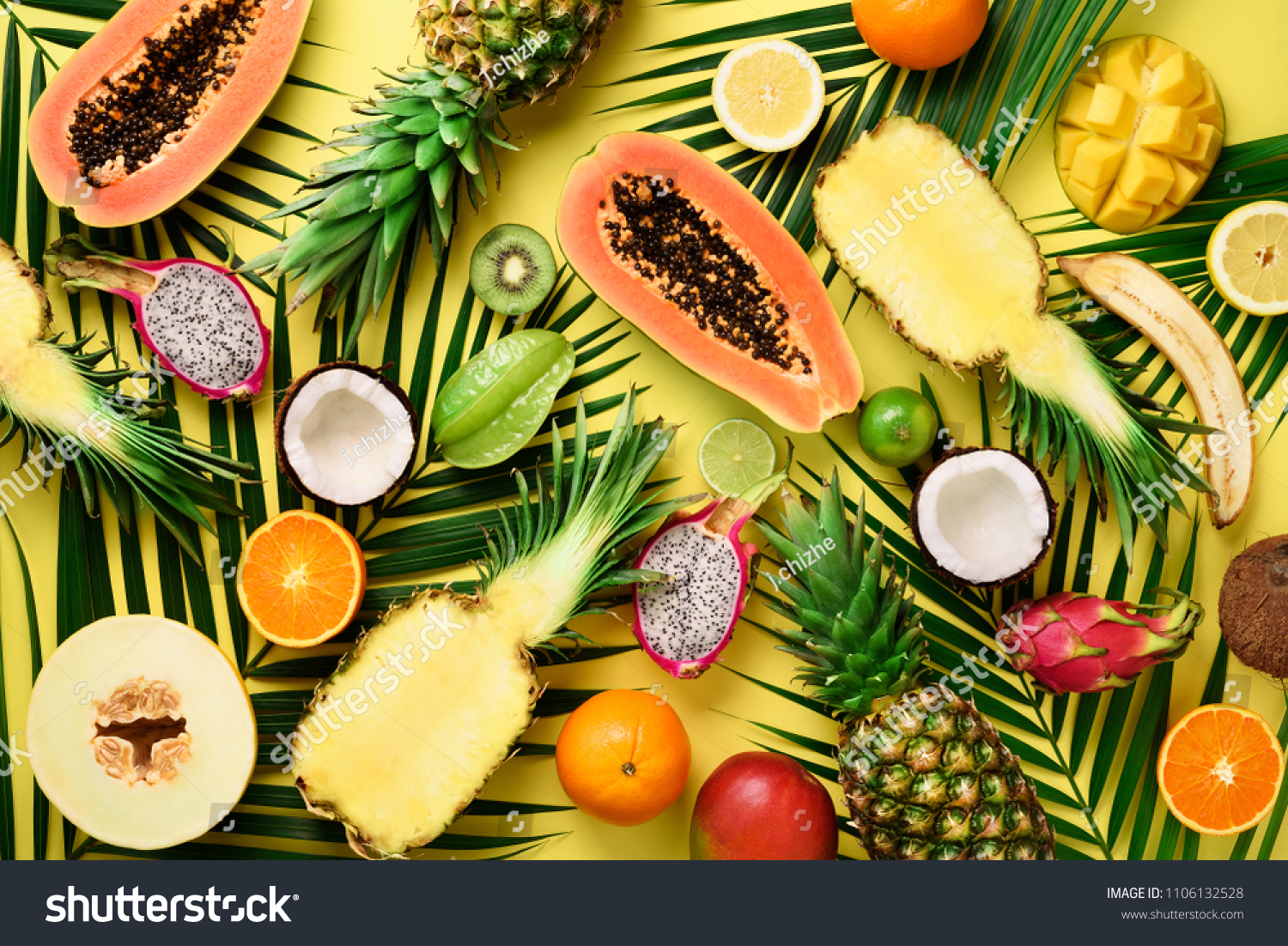 Exotic fruits and tropical palm leaves on pastel yellow background - papaya mango pineapple banana carambola dragon fruit kiwi lemon orange melon coconut lime. Top view