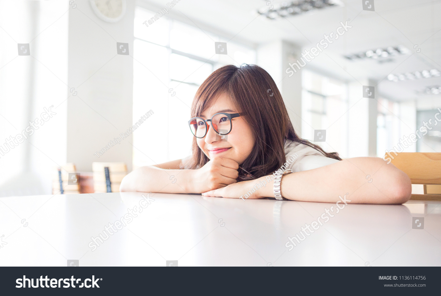 young female student is smiling with empty copy space on desk in library in campus of university