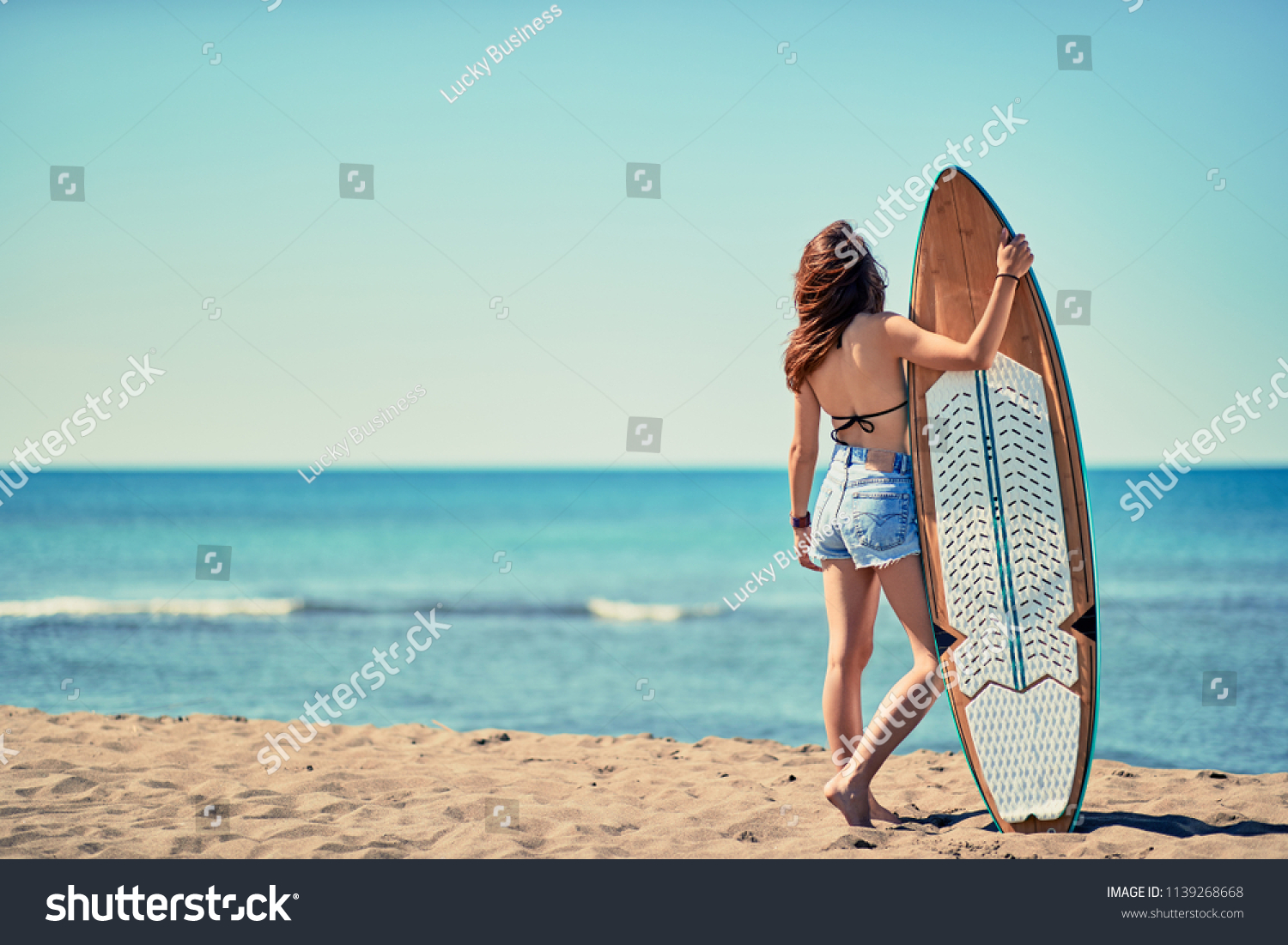 Young surfer girl at the beach with her surfboard looking for the waves