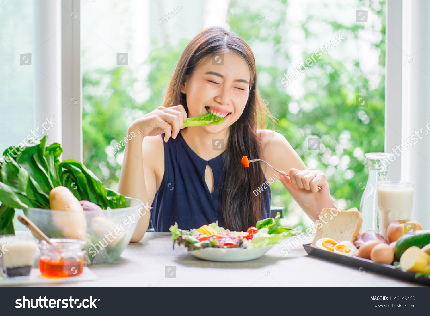 Young asian woman happy eating healthy salad sitting on the table indoors. Green healthy food concept.