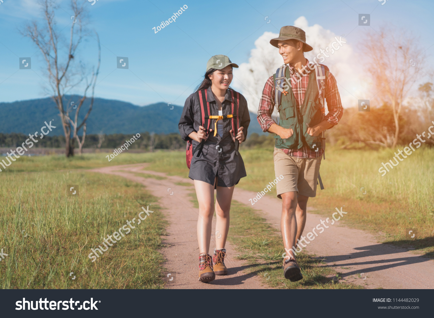 Hikings couple asian walking travel together at forest for camping on holiday weekend talking about something on the go near river and mountain view.