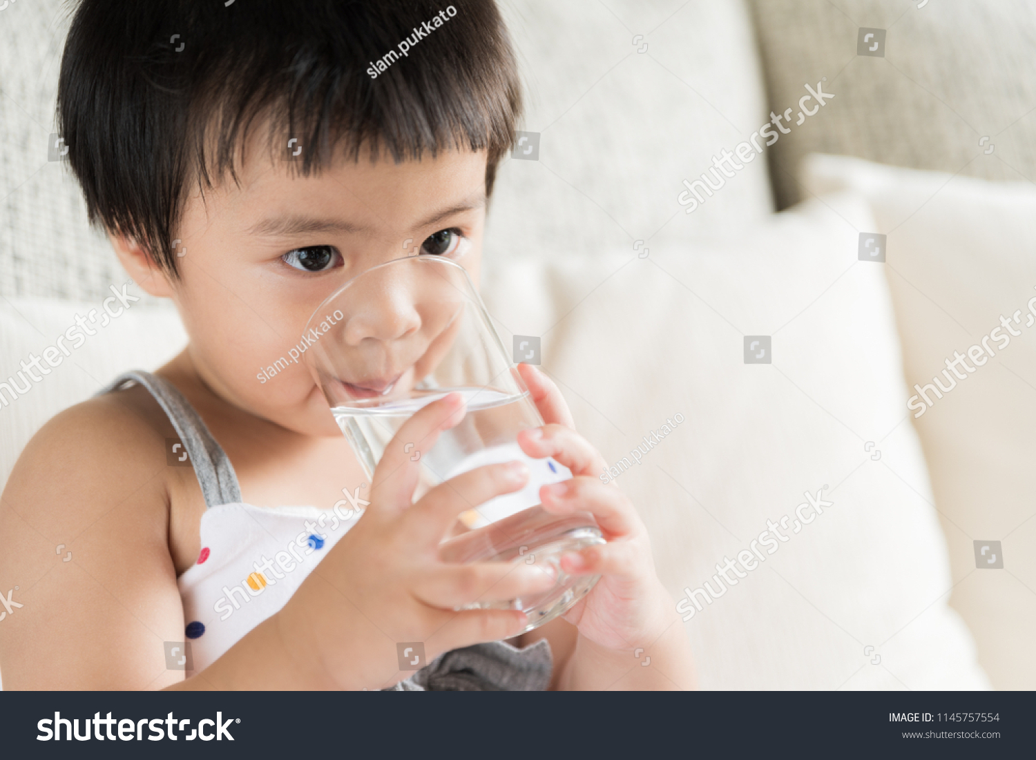 Cute little girl drinking water on sofa at home. health care concept.