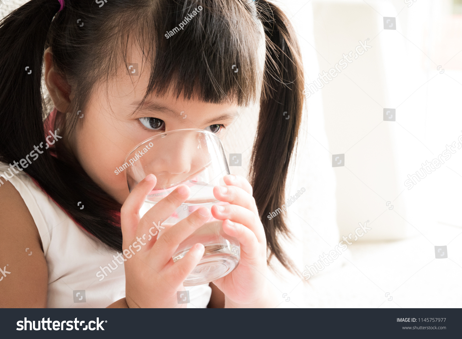 Cute little girl drinking water on sofa at home. health care concept.