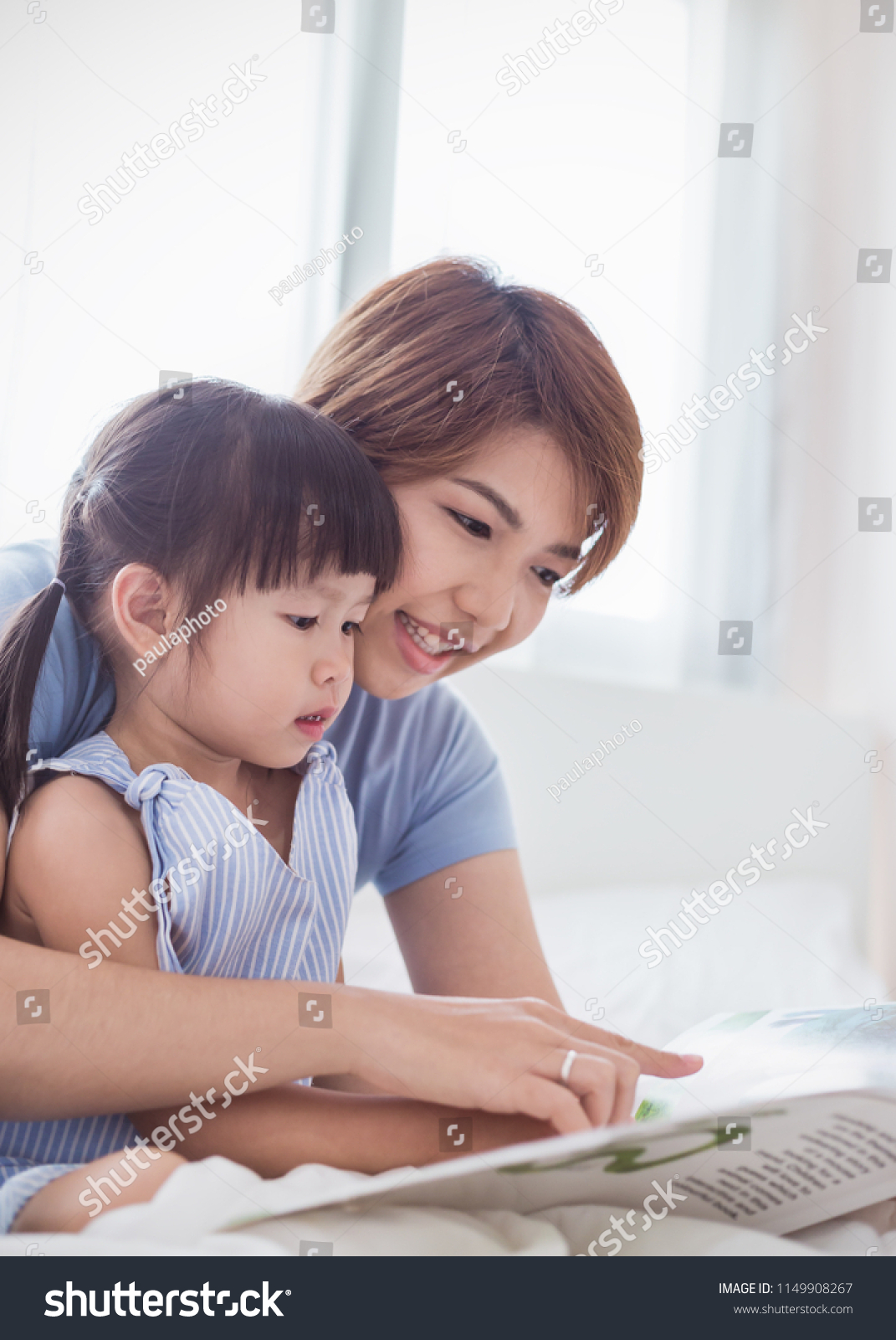 Portrait of beautiful asian mother hold story book reading teaching daughter little girl in bedroom. Home school learn from teacher education happy family love together mother’s day holiday concept.