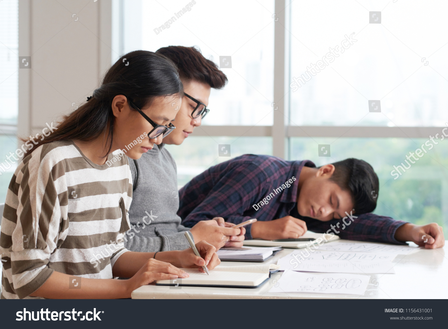 Vietnamese college student sleeping in class when his classmates writing in textbook or texting
