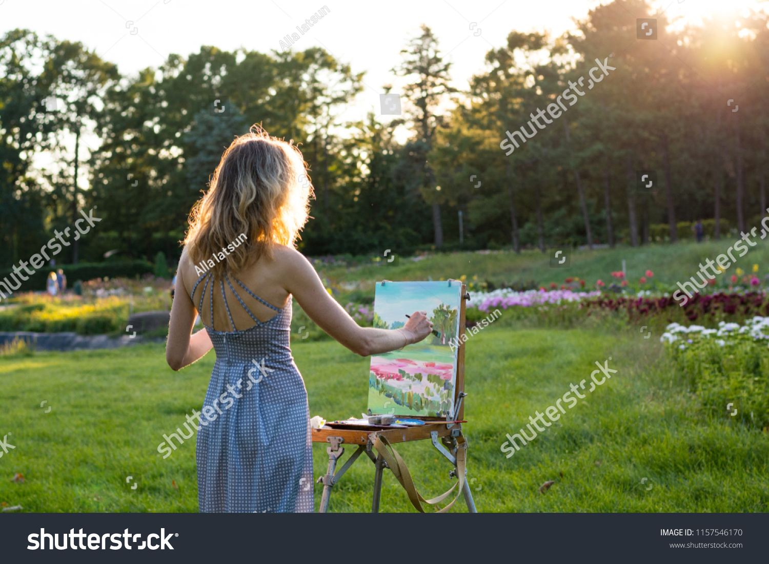 A young woman artist holds a brush and paints a picture on an easel in ...