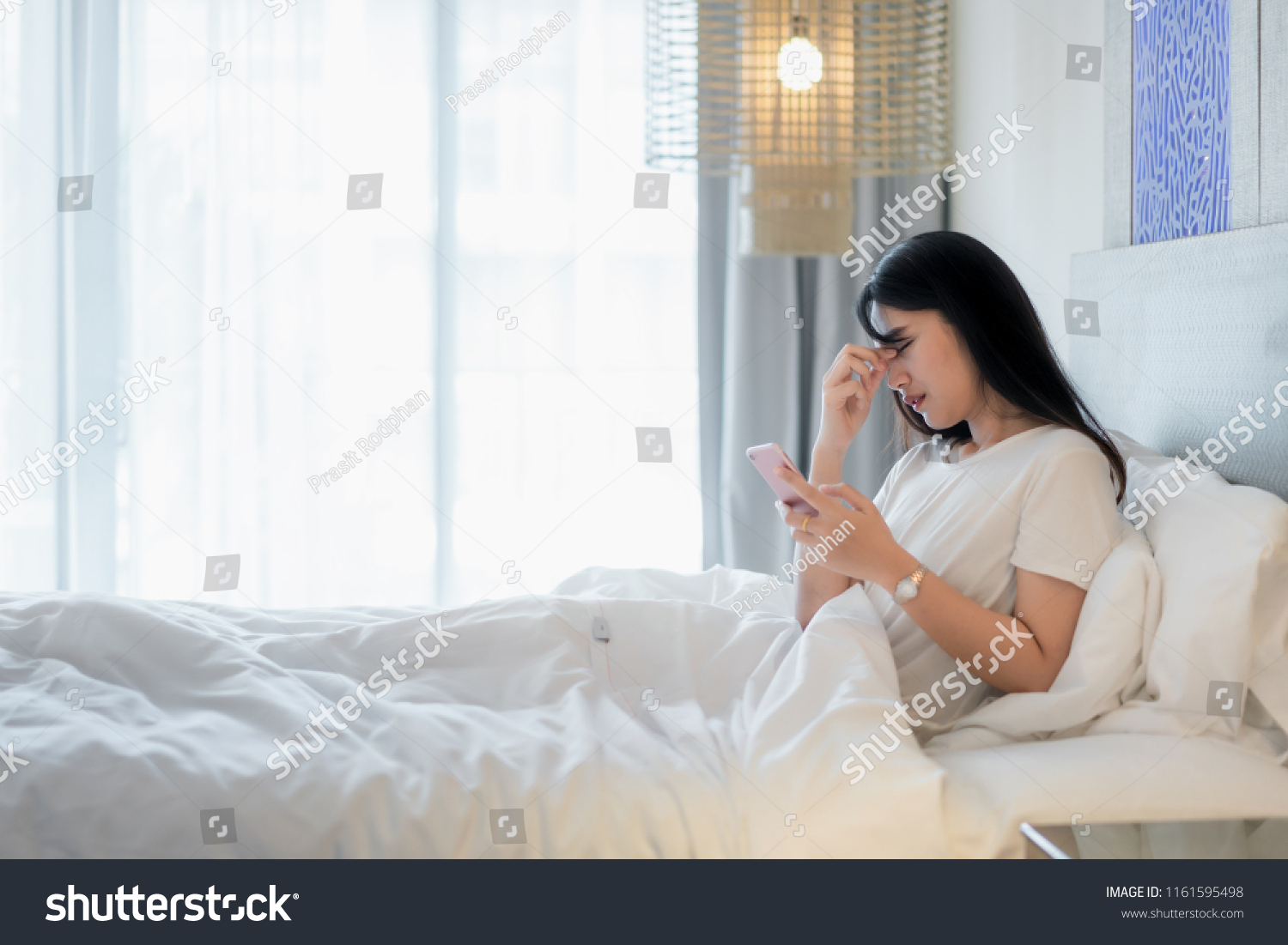 Asian woman in bed using mobile phone and feeling eye pain at bedroom in home.
