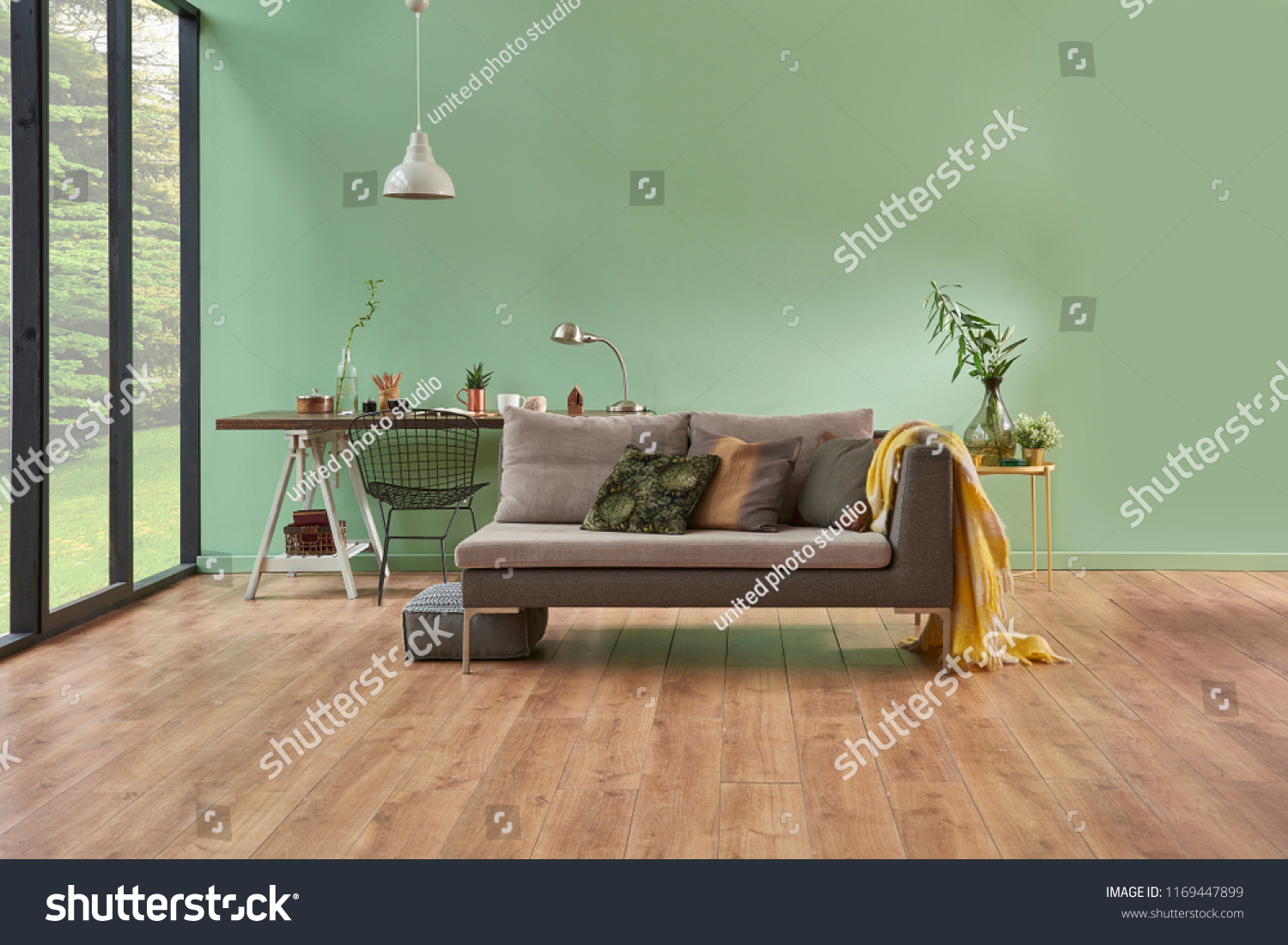 turquoise wall and living room. Grey sofa with yellow blanket and vase of flowers. Study table is on the back of sofa and decorative white lamp. empty area for carpet.