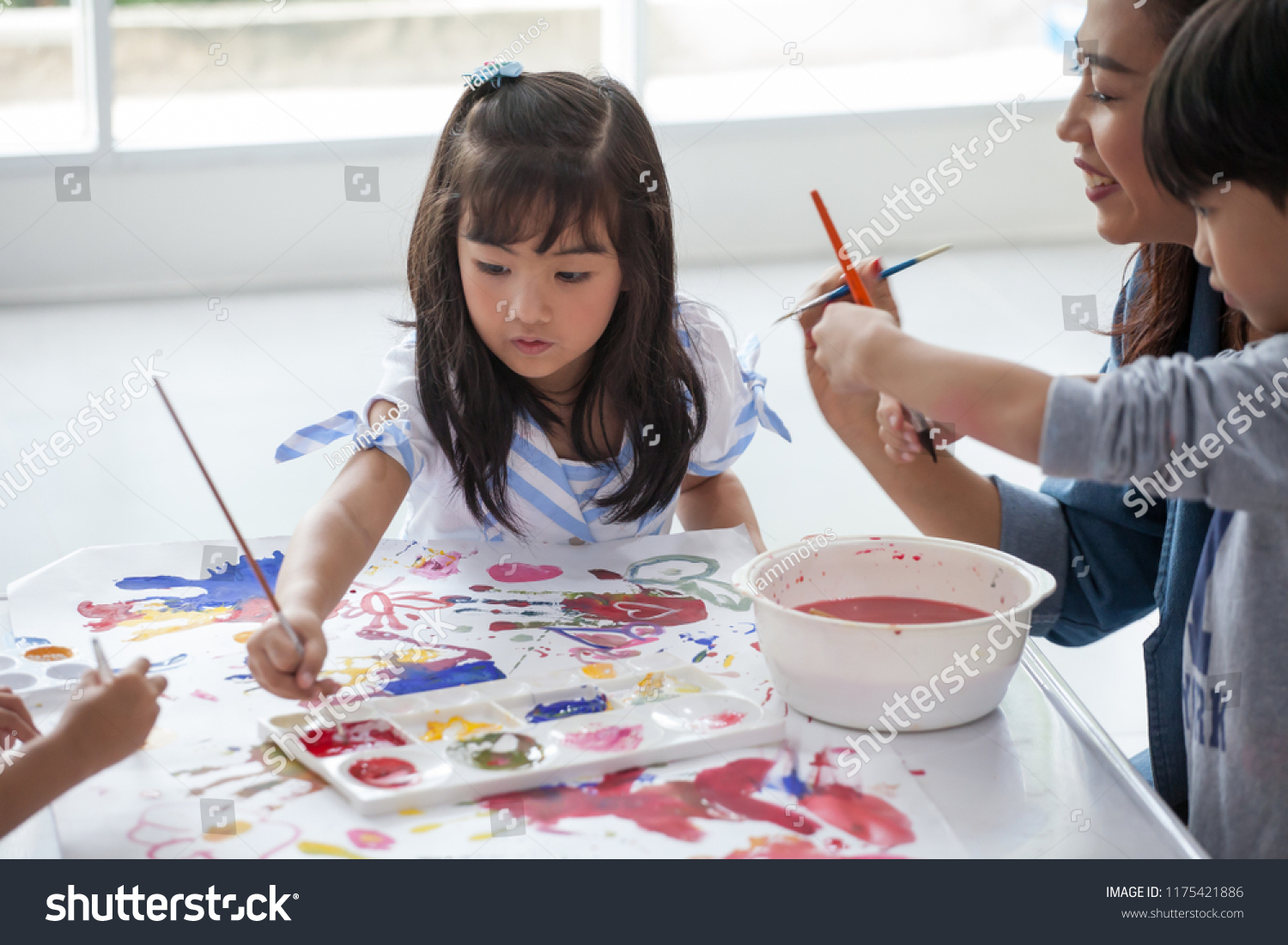 group of Cute little girl student painting  together with nursery teacher in classroom school . Happy children in a kindergarten
