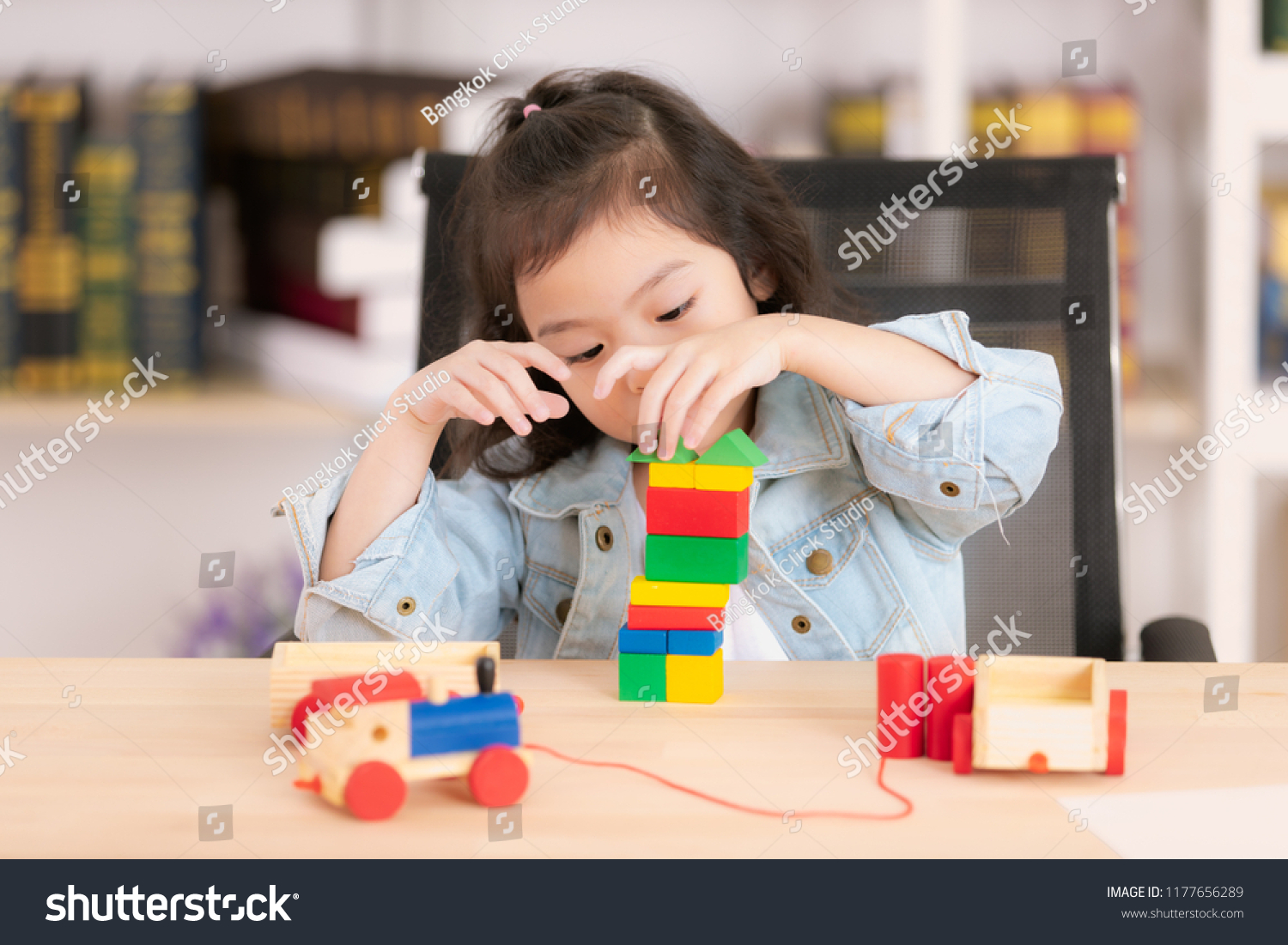 Lovely cute little Asian girl in jeans shirt concentrate  playing wood block toys on desk. Concept for funny activity of young kids in free time.
