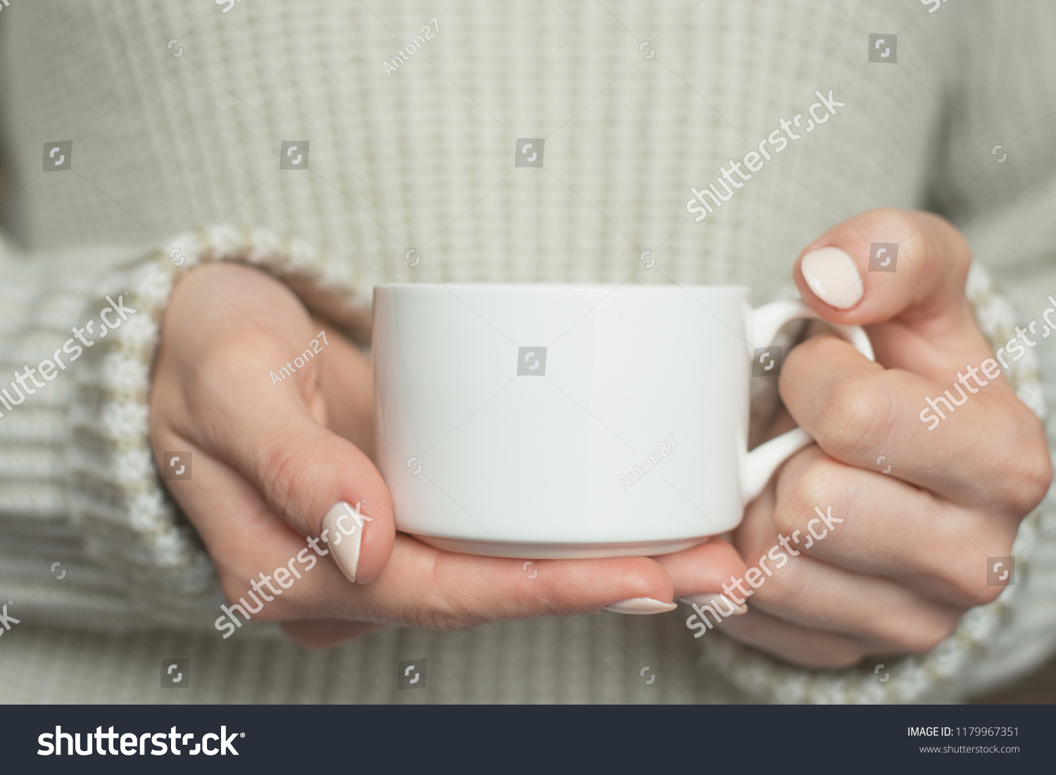 Girl in warm sweater is holding white mug in hands.. Mockup for winter gifts design.