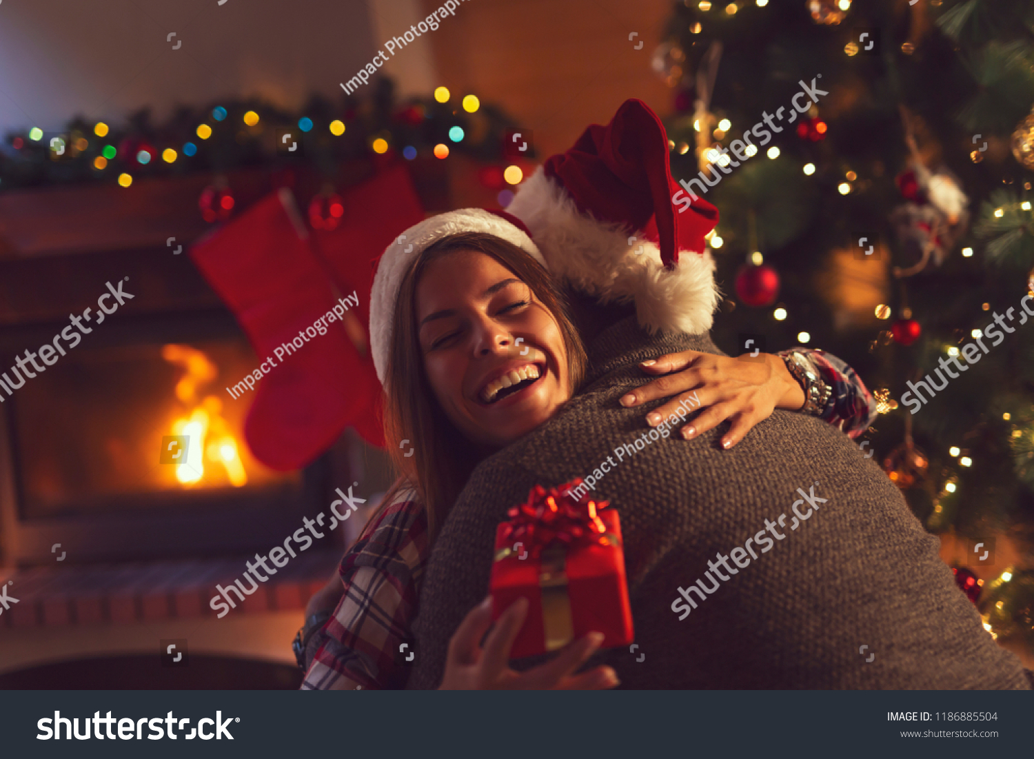 Young couple in love sitting by the fireplace and nicely decorated Christmas tree exchanging Christmas presents