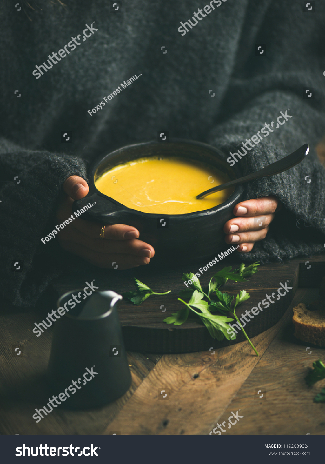 Woman in dark grey woolen winter sweater eating sweet corn and shrimp chowder soup from black bowl. Autumn or winter warming food
