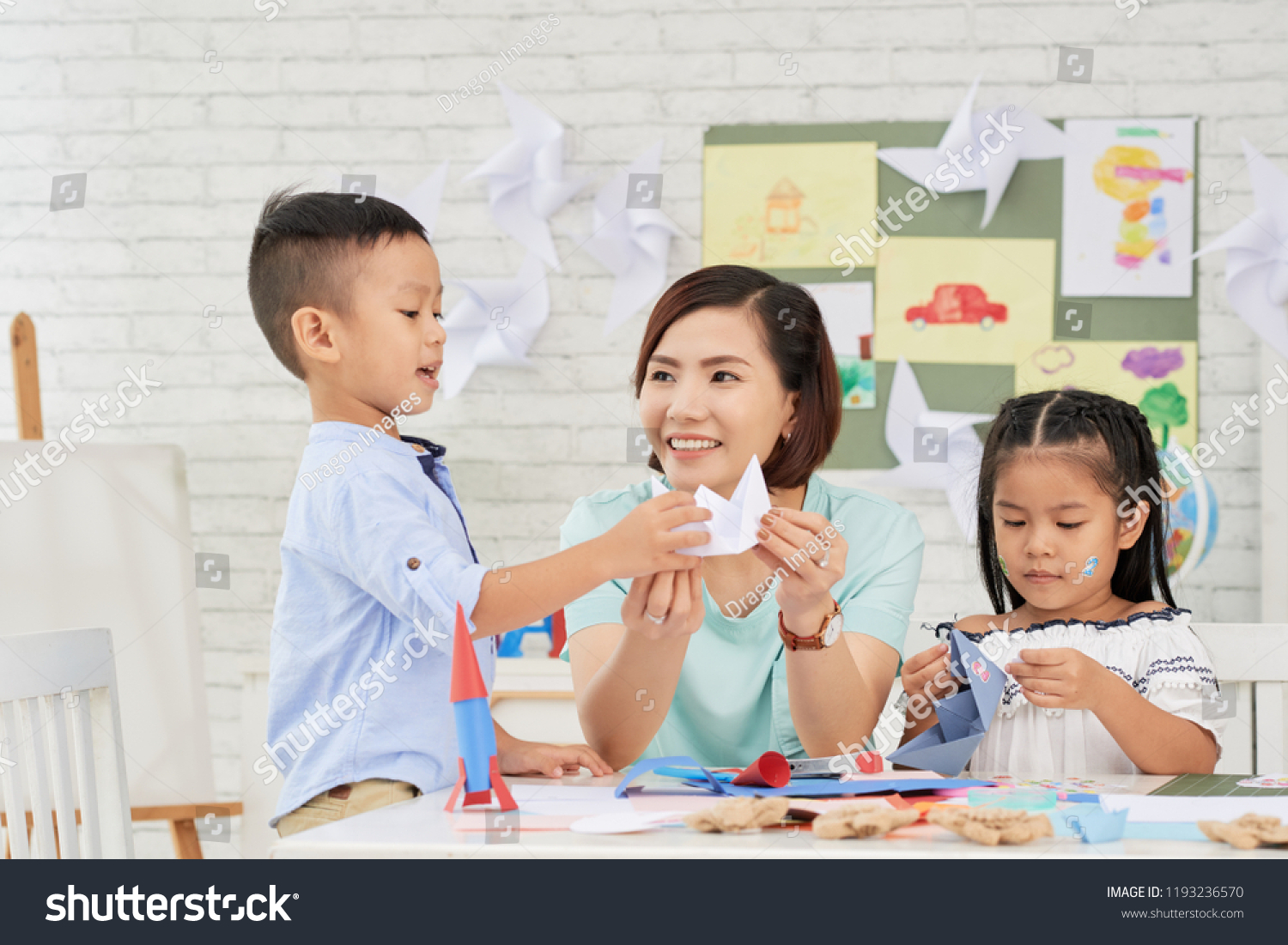 Young Asian woman teaching children how to make paper ships at art craft