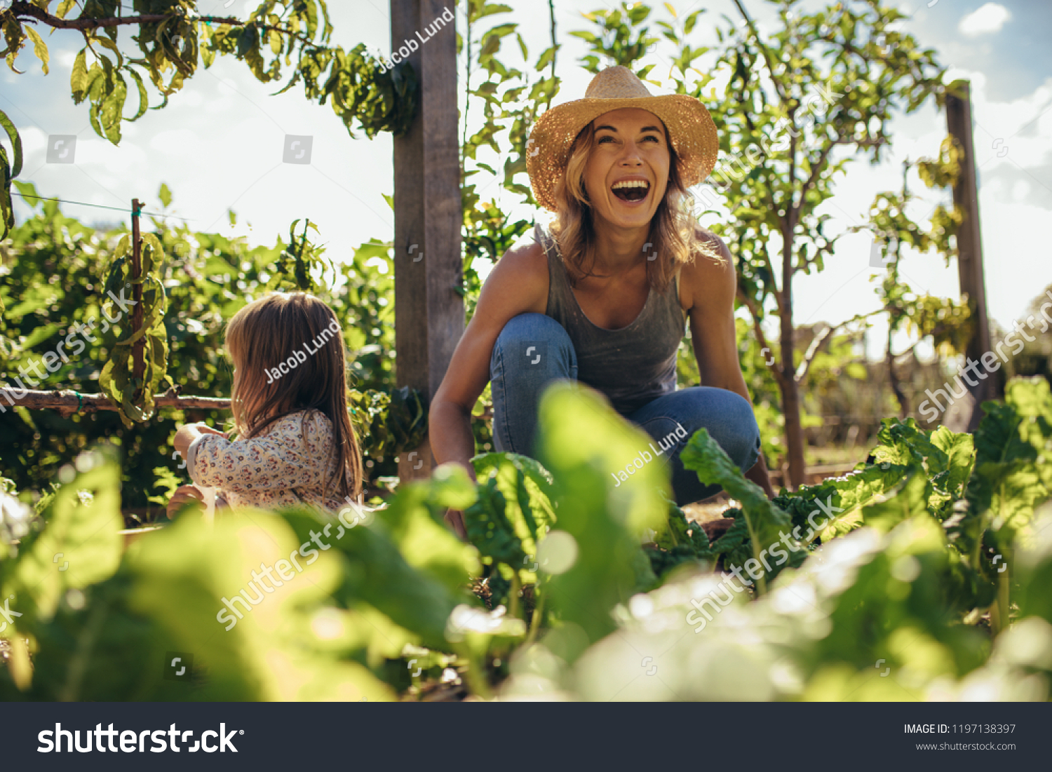 Beautiful young female farmer working in her garden with her daughter sitting by. Young mother and daughter working in the farm.