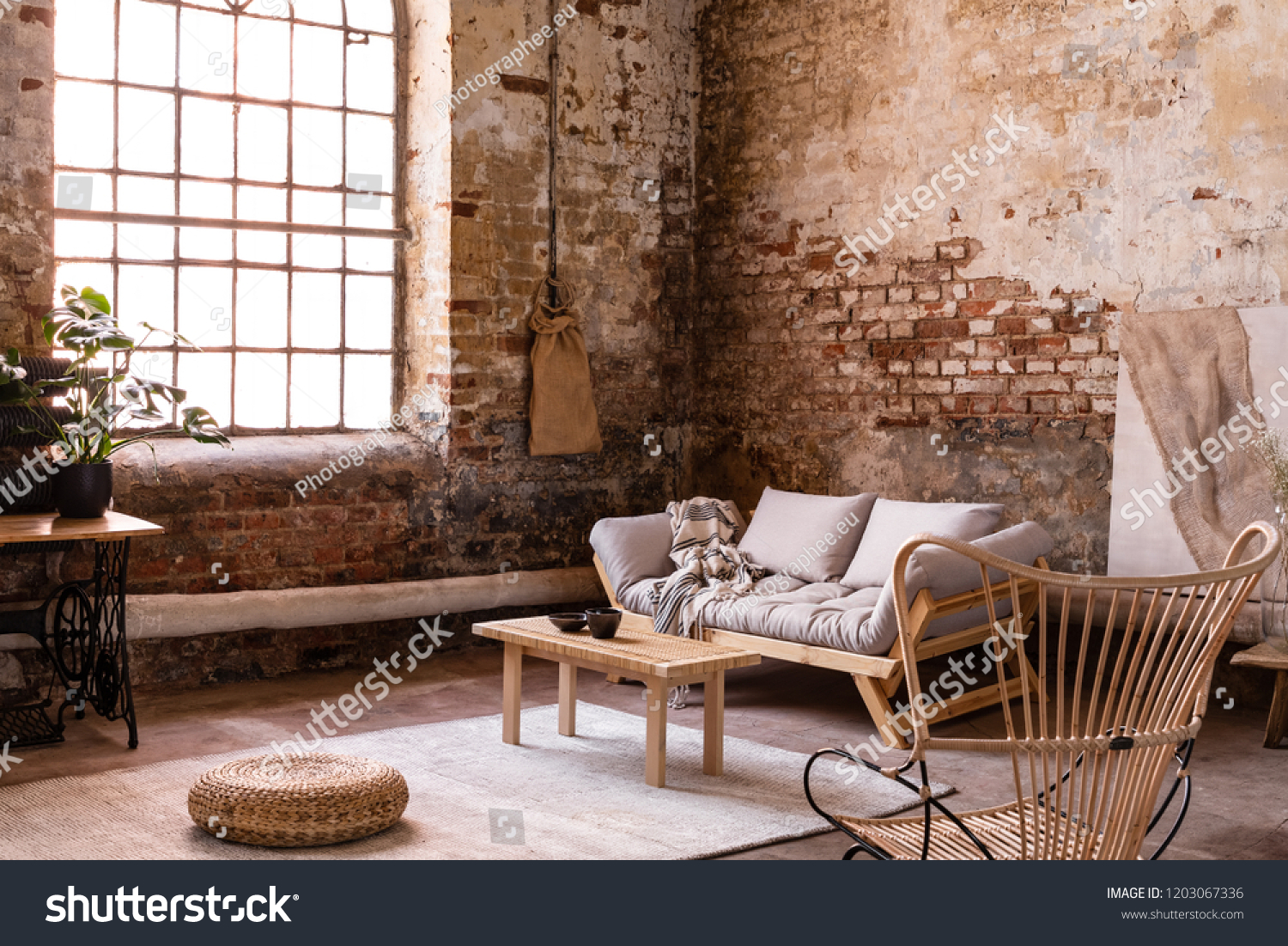Pouf and wooden table on carpet near window in bright wabi sabi interior with sofa and armchair. Real photo