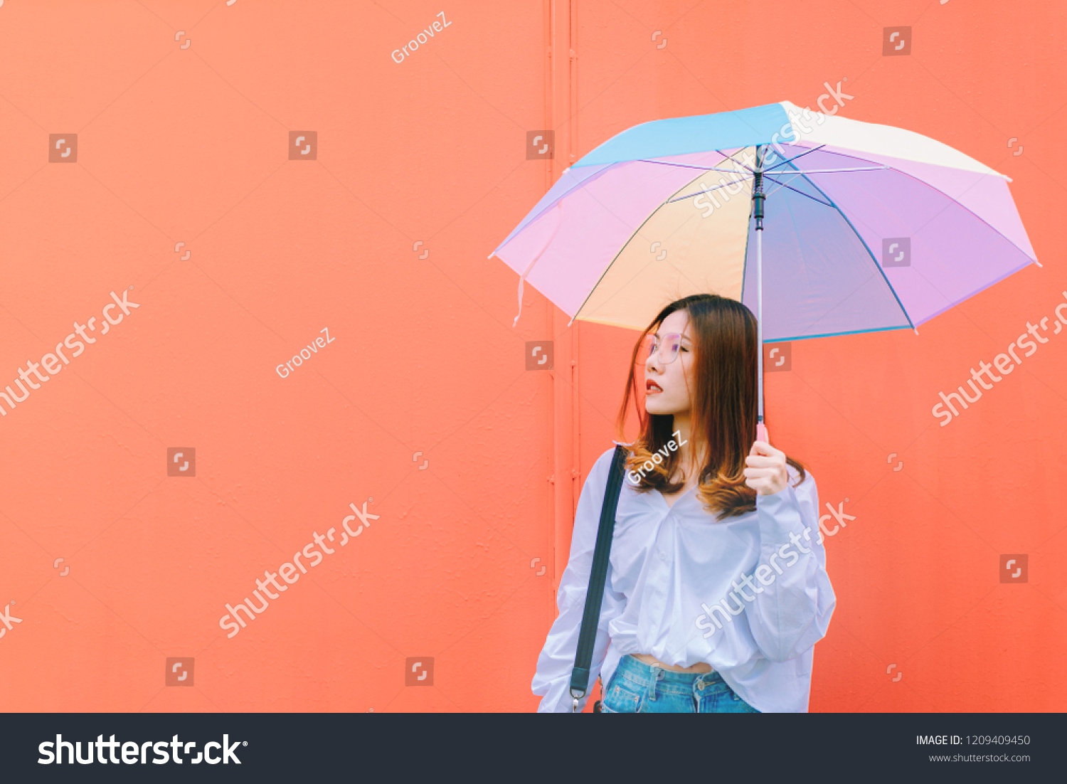 Asian woman with colorful umbrella on red wall background.