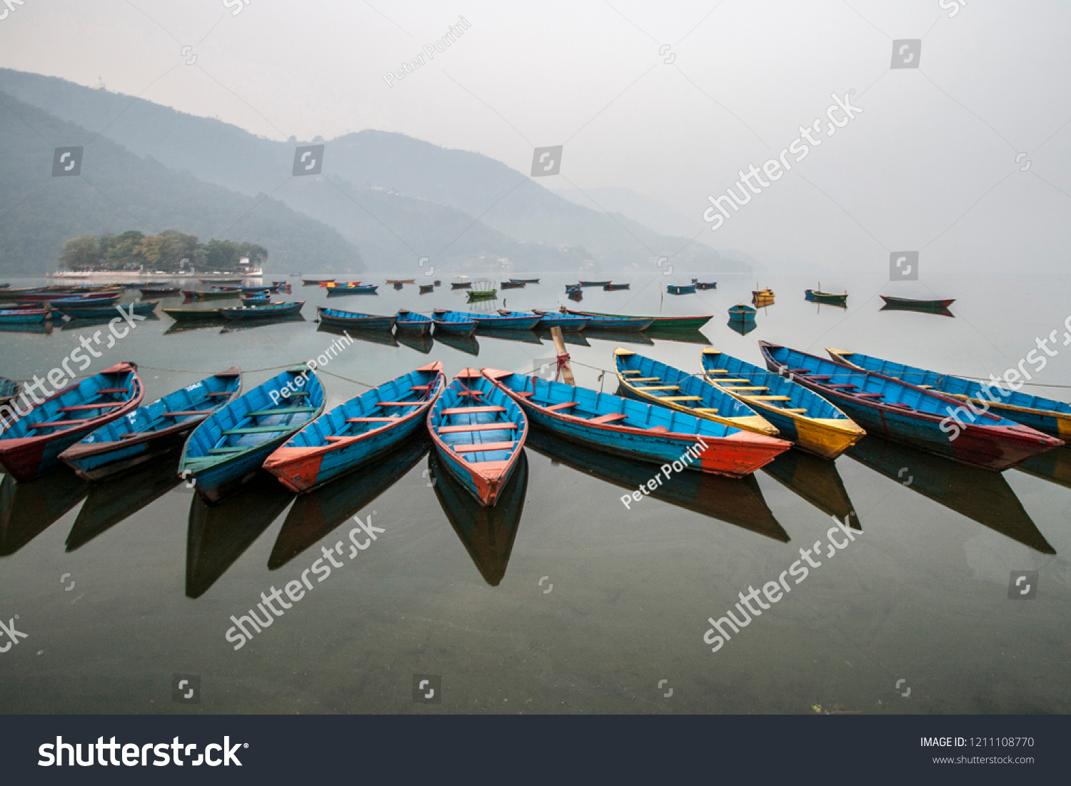 Colourful boats at shore of beautiful Phewa lake with misty landscape on background. Pokhara Nepal