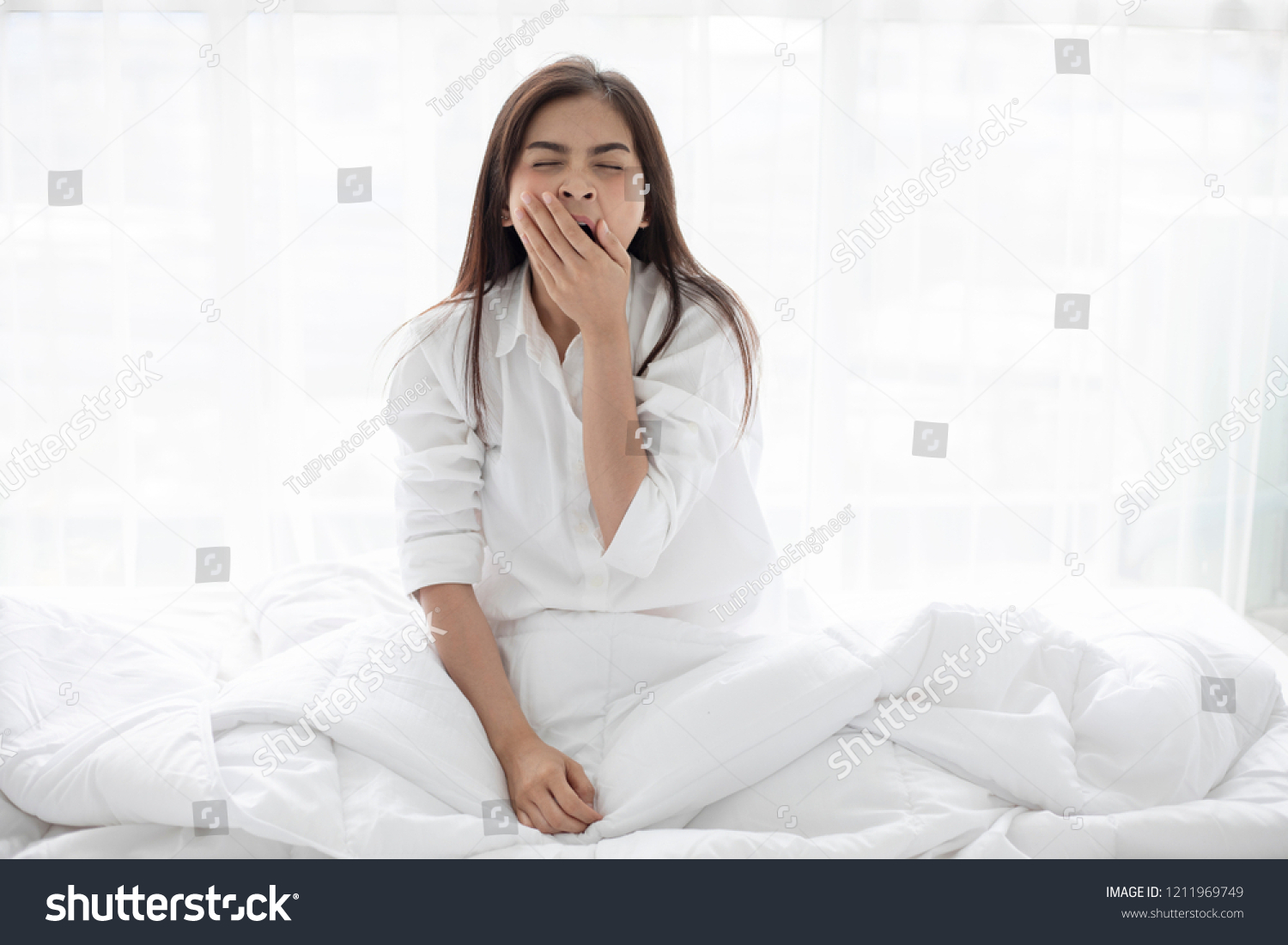 Asian woman Beautiful young smiling woman sitting on bed and stretching in the morning at bedroom after waking up in her bed fully rested and open the curtains in the morning to get fresh air.