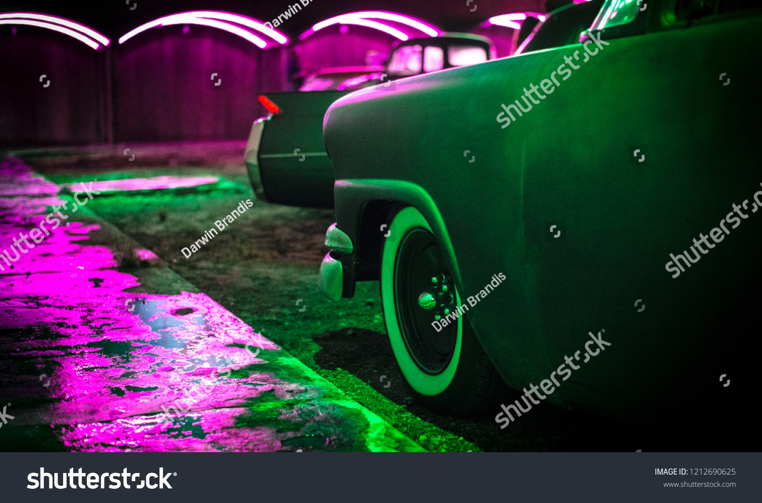 Classic American cars are bathed in colorful neon lights. 