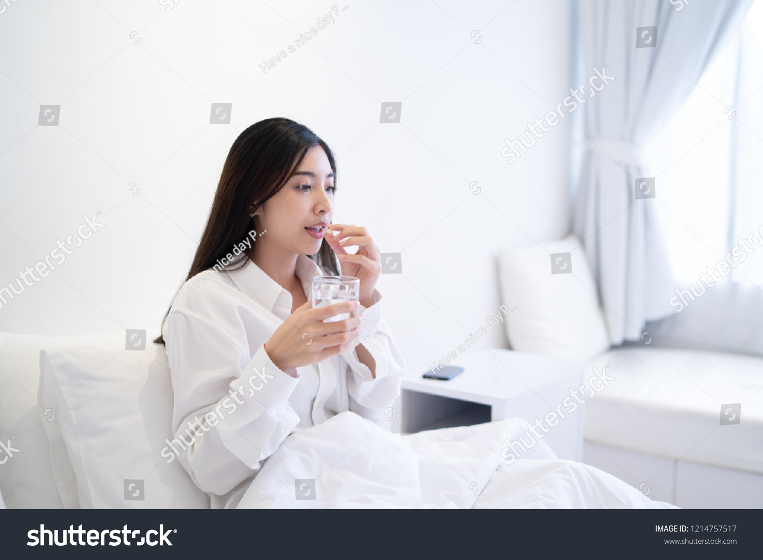 Young Thai girl Business woman taking medicine and drinking water holding pills glass of water on bed in hospital bedroom she work hard while feels sick drug remedy health care Medical people concept