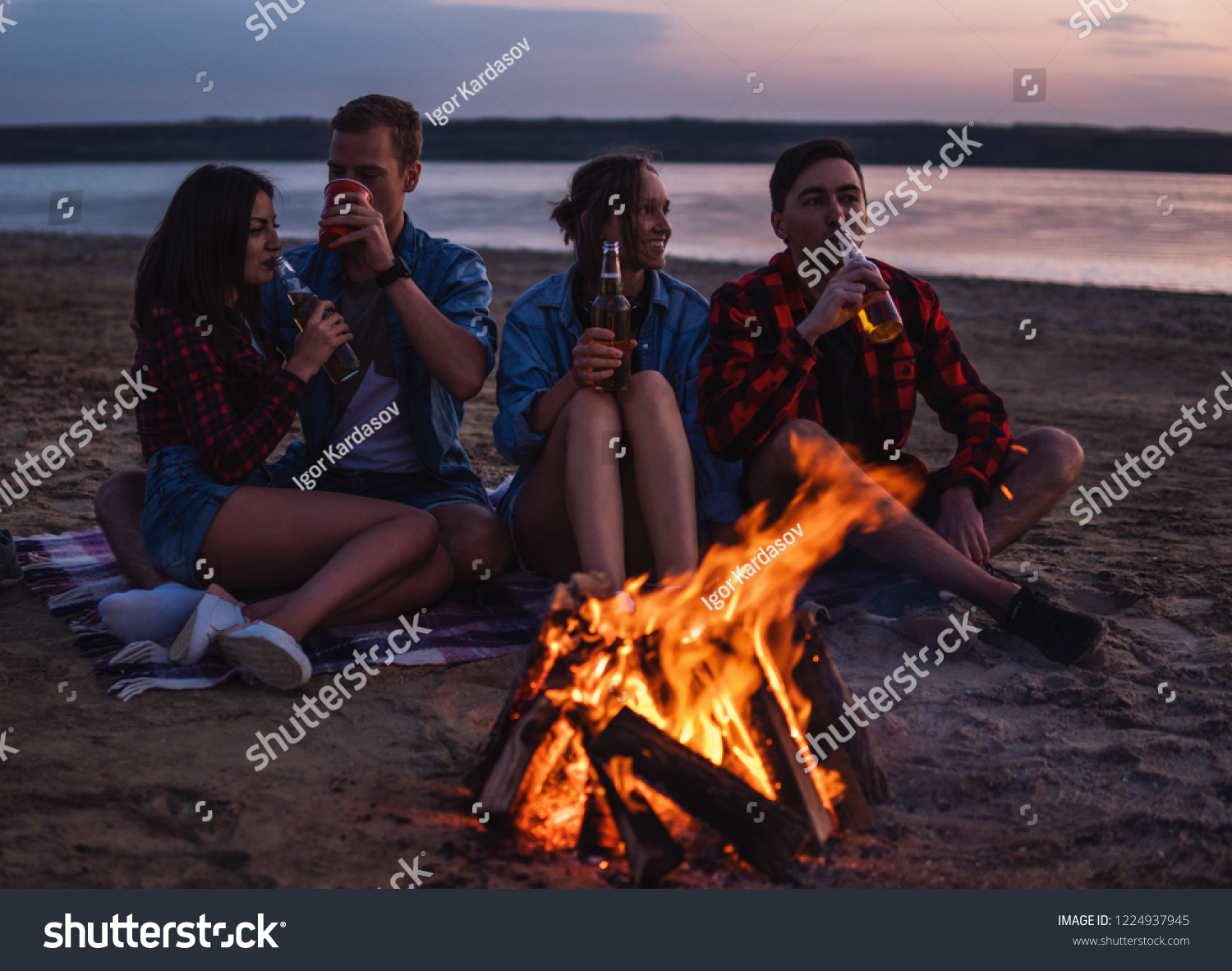 Camp on the beach. Group of young friends having picnic with bonfire. They drink beer