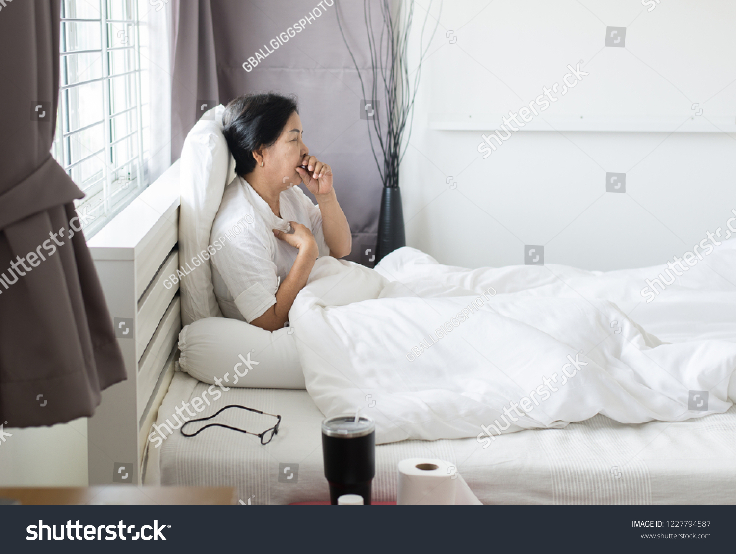 Elderly asian woman coughing and sitting on her bed Concept of health