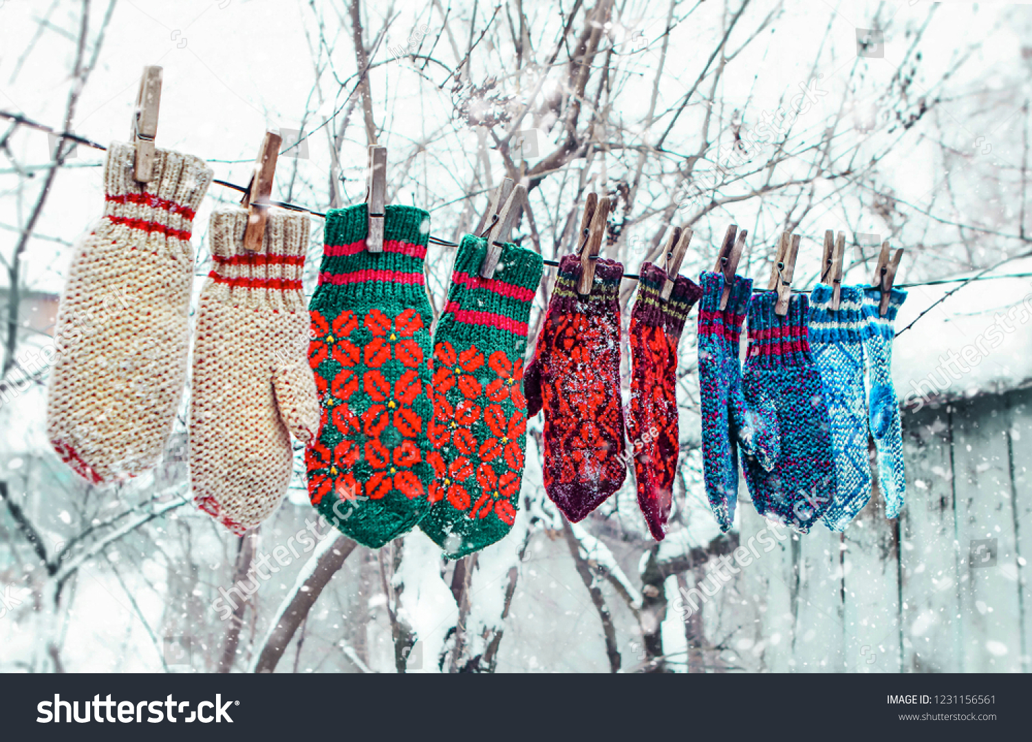 knitted mittens on natural winter background.  color mittens hanging by thread in winter day under the falling snow. Winter season symbol.
