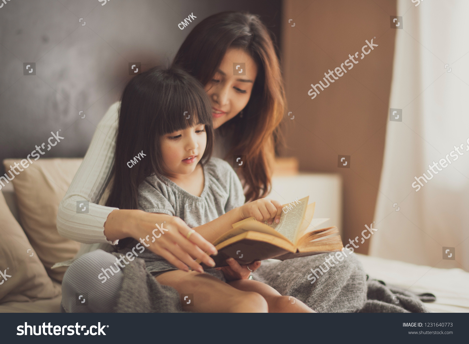 Love of young mother and daughter. Teaching reading a book on the bed at home. mother and daughter look at the book feel good and happy