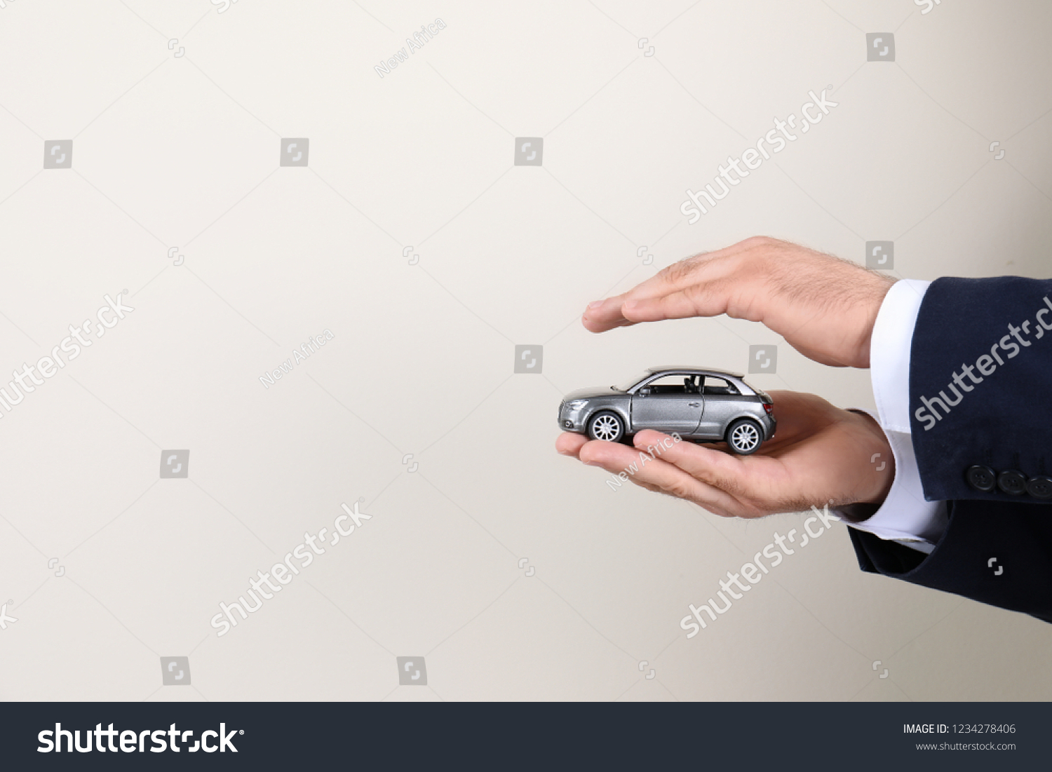 Male insurance agent holding toy car on light background  closeup. Space for text