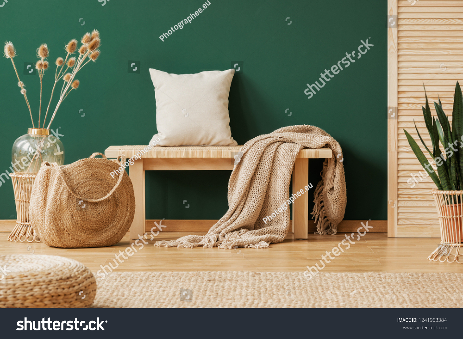 Blanket and pillow on wooden bench in green apartment interior with pouf bag and plants. Real photo