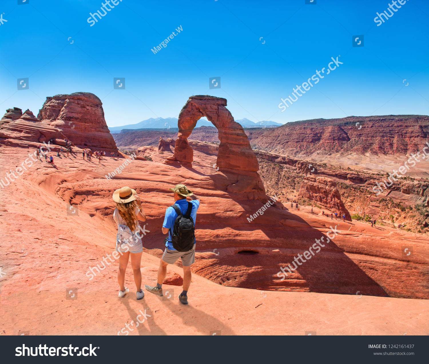 Couple on vacation hiking trip. Man and woman standing on top of the mountain looking at beautiful view. Delicate Arch Moab Utah Arches National Park.