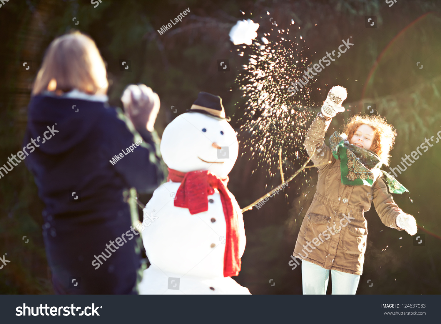 Two girls having snowball fight. One of them throwing snowball is in focus  motion blur