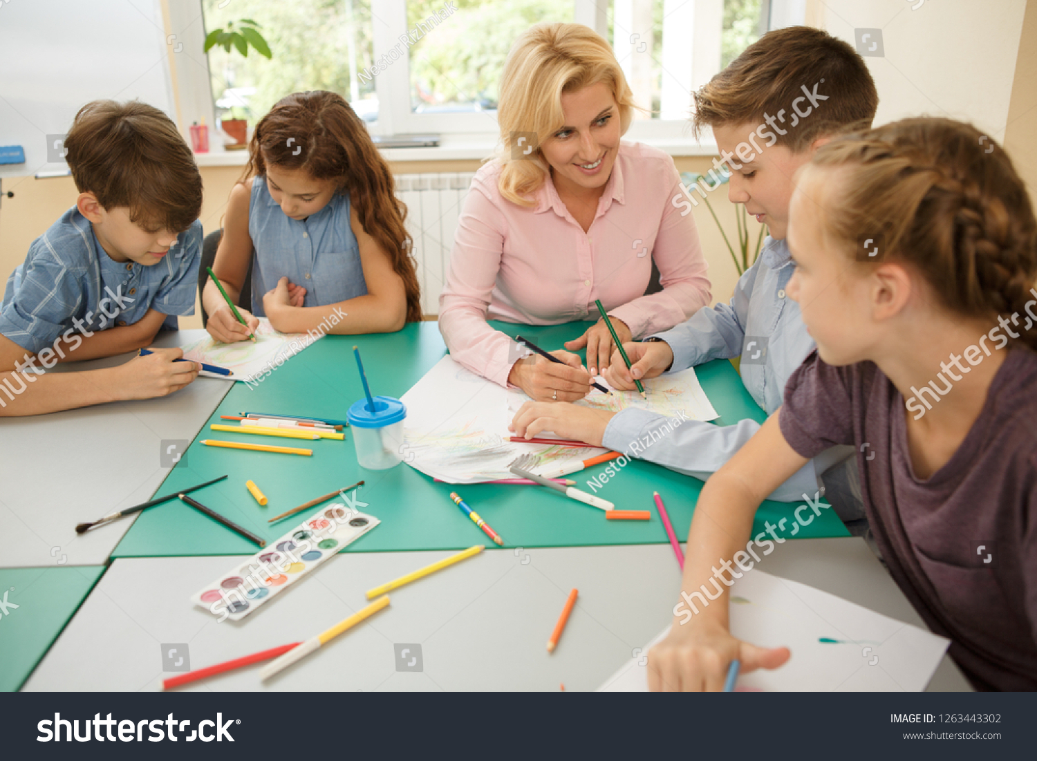 Group of children with female teacher sitting and painting on paper at ...