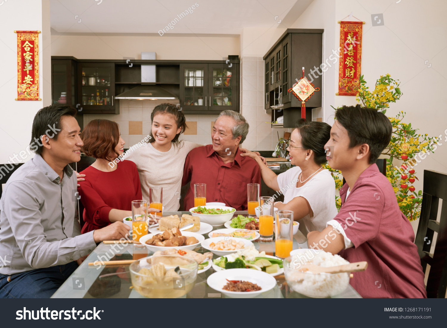Happy big Asian family sitting at dinner table and celebrating Lunar New Year  couplets with best wishes for coming year in the background