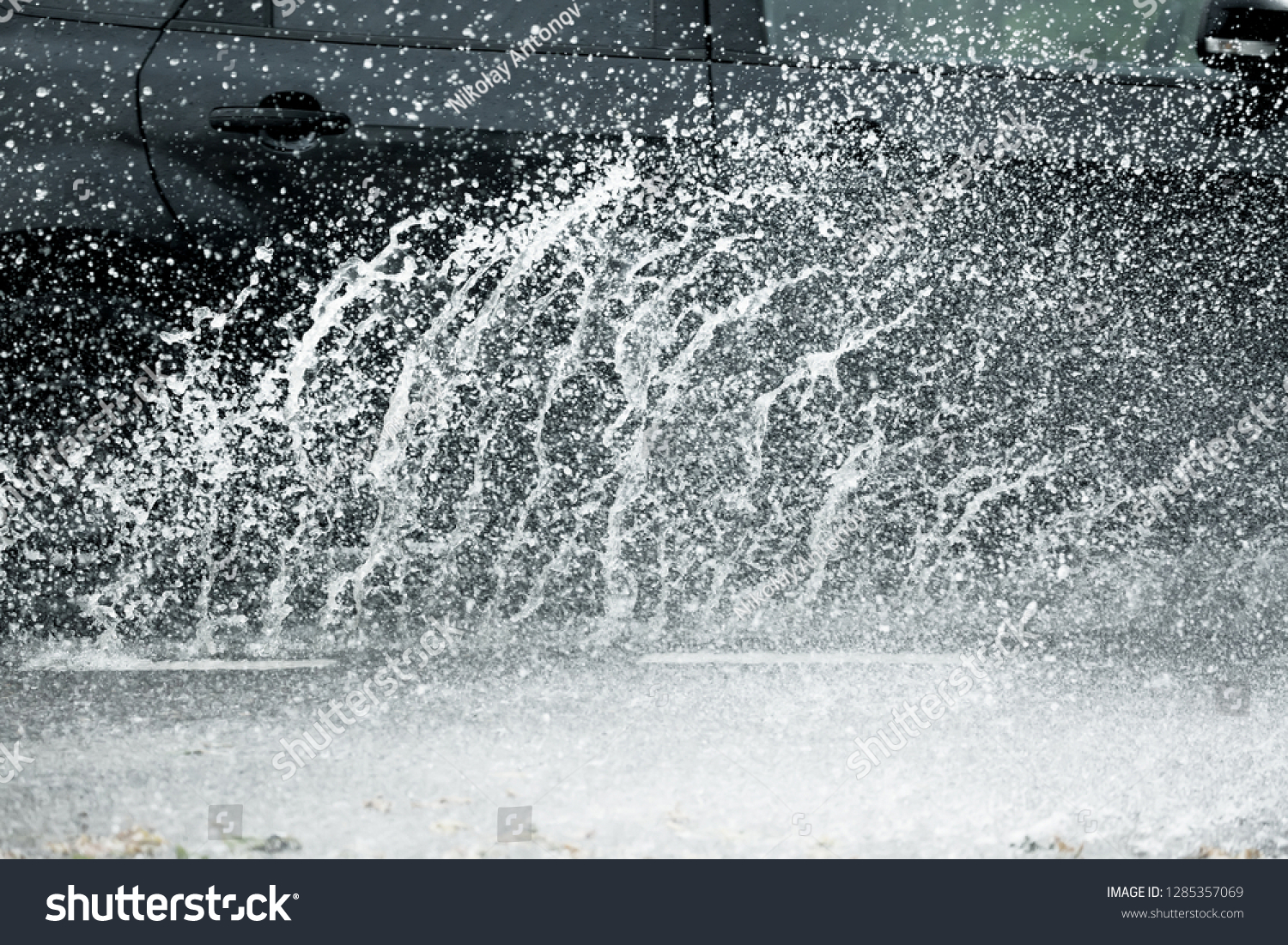 Car motion through big puddle of water splashes from the wheels on the street road. Water splash rain texture