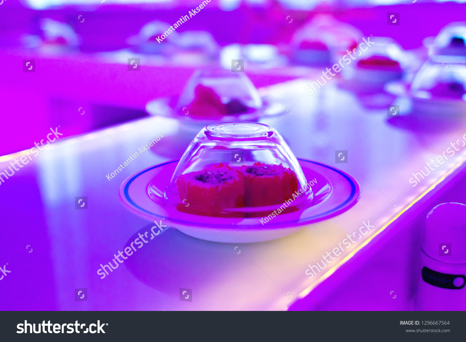 Conveyor serving dishes. Neon-purple lights over the plates with the sushi rolls.