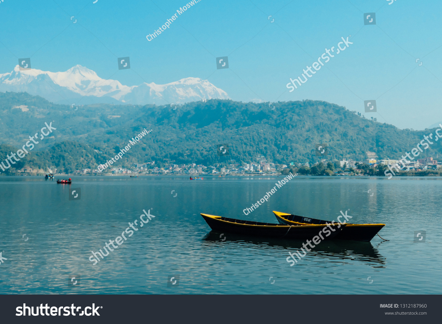 Two empty boats floating on the surface of Phewa Lake Pokhara Nepal. IN the back more boats with tourists. Cityscape on the shore. High Himalayan peaks in the back. Chilled and relaxed atmosphere.