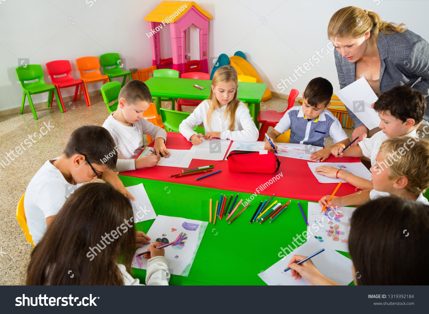 happypositivefemaleteacherhelpingschoolkidsdrawingwithc