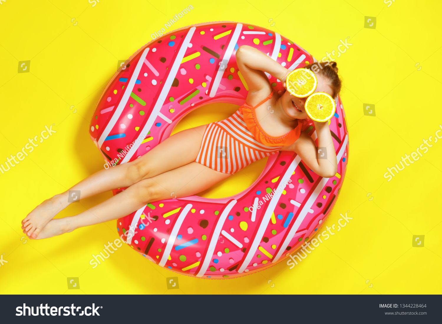 A little child girl in a swimwear suit lying on a donut inflatable circle. Yellow background. Top view. Summer concept.