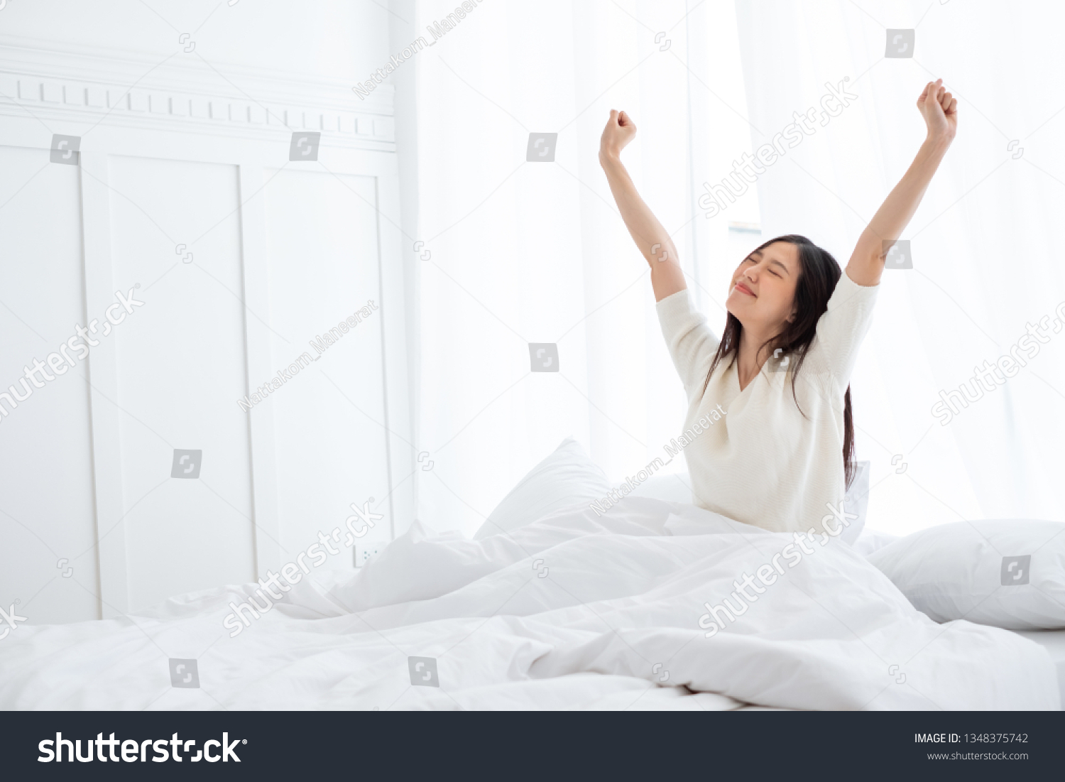 Asian woman wake up in the morning sitting on white bed and stretching feeling happy and fresh