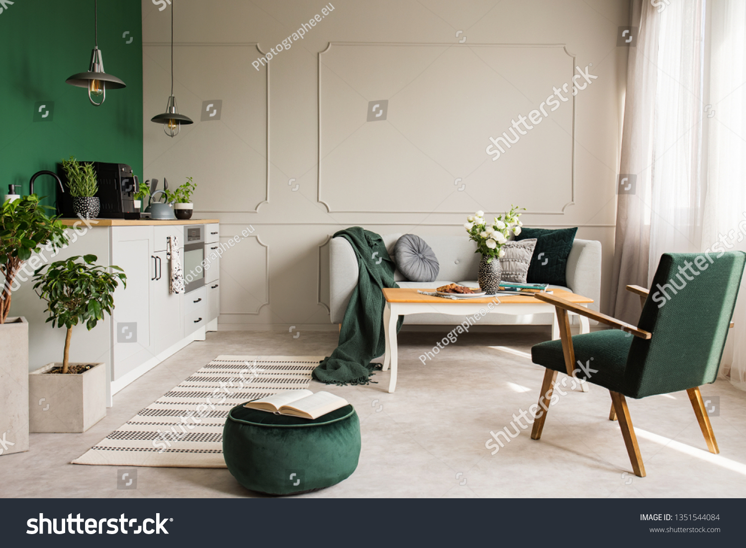 Open book on dark green velvet pouf in grey living room and kitchen interior with retro armchair coffee table and sofa