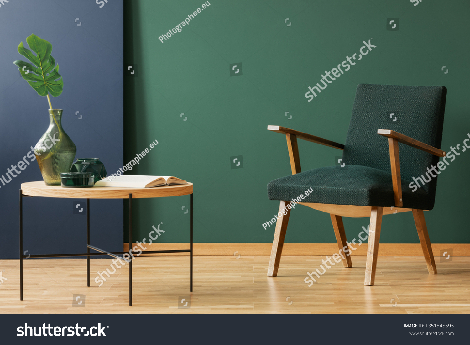 Wooden armchair next to table with leaf and book in green and blue living room interior. Real photo